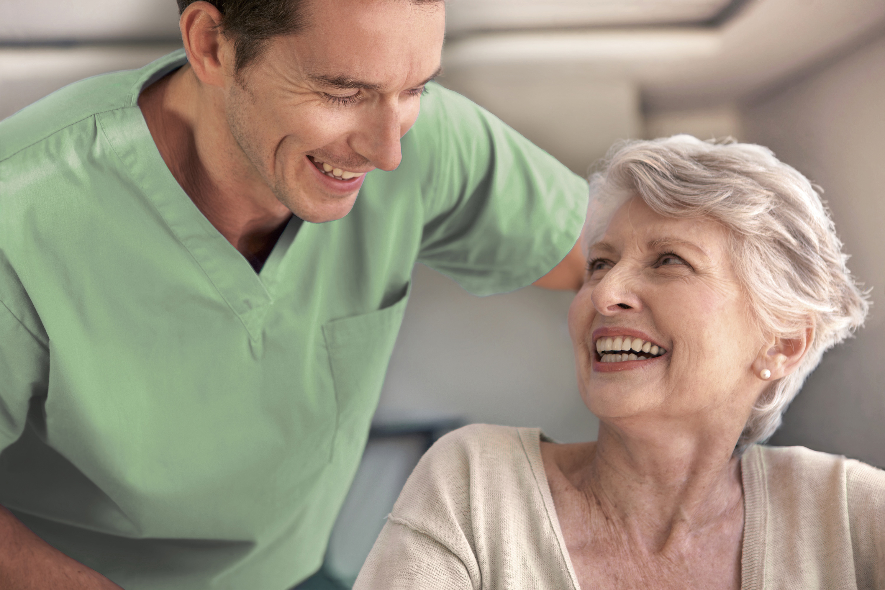 nuvie-Pflegekraft und lachende Seniorin im Gespräch
